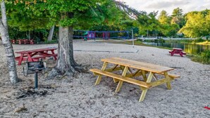 Ein Sandstrand mit Picknicktischen, einem Grill und einem Spielplatz im Hintergrund.