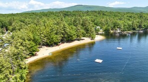 Un lago rodeado de un bosque denso, una playa arenosa y algunas embarcaciones.