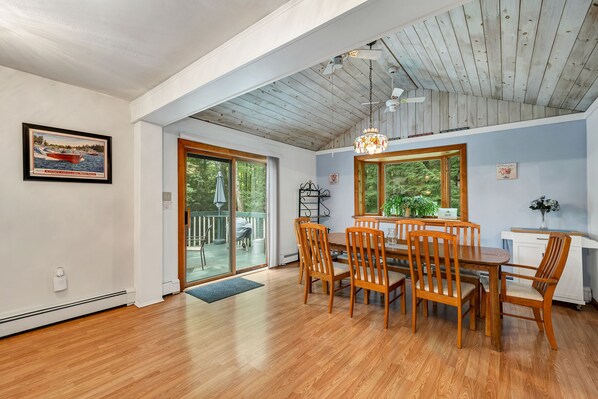 A dining area with a wooden table and chairs, a ceiling fan, and a view of the outdoors through large windows.