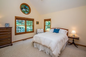 Quarto com cama grande, duas janelas, cômoda, mesa de cabeceira com abajur e vitral.