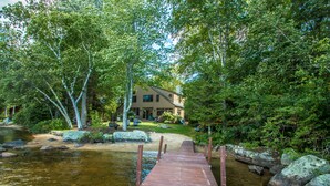 A wooden dock leading to a house surrounded by trees and a body of water.