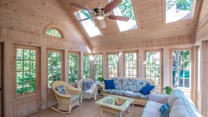 A spacious room with a high ceiling, large windows, a ceiling fan, and a variety of seating options including a sofa, chairs, and a small table.