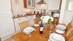 A dining area with a wooden table set for four, white plates, cutlery, and a bottle of wine. - 8 Munday Cottages (Yarmouth)