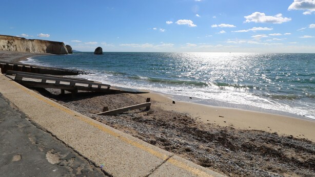 A coastal beach with a concrete walkway, rocky shore, and cliffs in the background. - 8 Munday Cottages (Yarmouth)