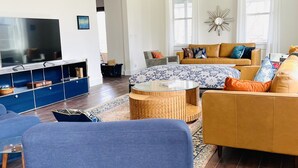A modern living room with a large TV, comfortable seating, a coffee table, and a chandelier. - Magnificent Modern Farmhouse (Mountain Dale)