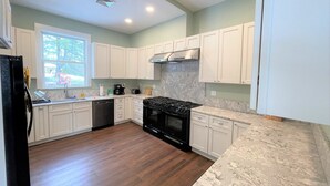 A modern kitchen with white cabinets, a black stove, and a marble countertop. - Magnificent Modern Farmhouse (Mountain Dale)