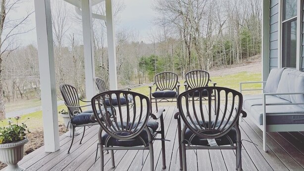 A covered outdoor seating area with wooden flooring and metal chairs. - Magnificent Modern Farmhouse (Mountain Dale)