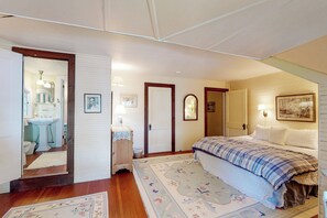 Quarto com uma cama, mesa de cabeceira, espelho, porta e banheiro visível por uma porta aberta.