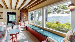 A cozy room with a large window overlooking a body of water, wicker furniture, and a wooden ceiling. - Lake Winnipesaukee Waterfront Rental Wolfeboro NH Dock Sleeps 13 (Wolfeboro)