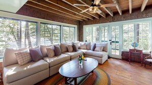 A spacious living room with a large sectional sofa, a wooden ceiling, and large windows offering a view of trees. - Lake Winnipesaukee Waterfront Rental Wolfeboro NH Dock Sleeps 13 (Wolfeboro)