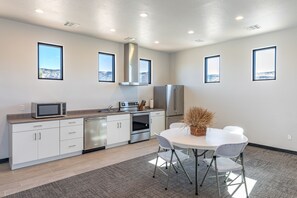 A modern kitchen with white cabinets, stainless steel appliances, and a dining area with a table and chairs. - Golfside 4BR - 3 King Suites, w/ Hot Tub & Firepit (St. George)