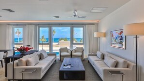 A spacious living room with a large window overlooking the ocean, a coffee table, sofas, and a dining area with a view. - ☀️👙Sea Fan by IRE Vacations - Exquisite Villa With Views from Each Bedroom (Oyster Pond)