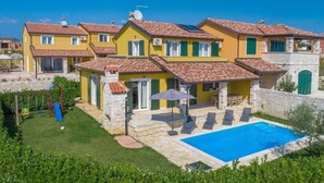 Una villa amarilla con piscina, muros de piedra y zona de juegos infantiles.