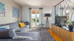 Una sala de estar moderna con un sofá gris, una mesa de centro, un televisor y un amplio ventanal con cortinas.