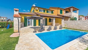 Una casa de dos plantas con piscina, escalones de piedra y una zona de juegos con un tobogán.
