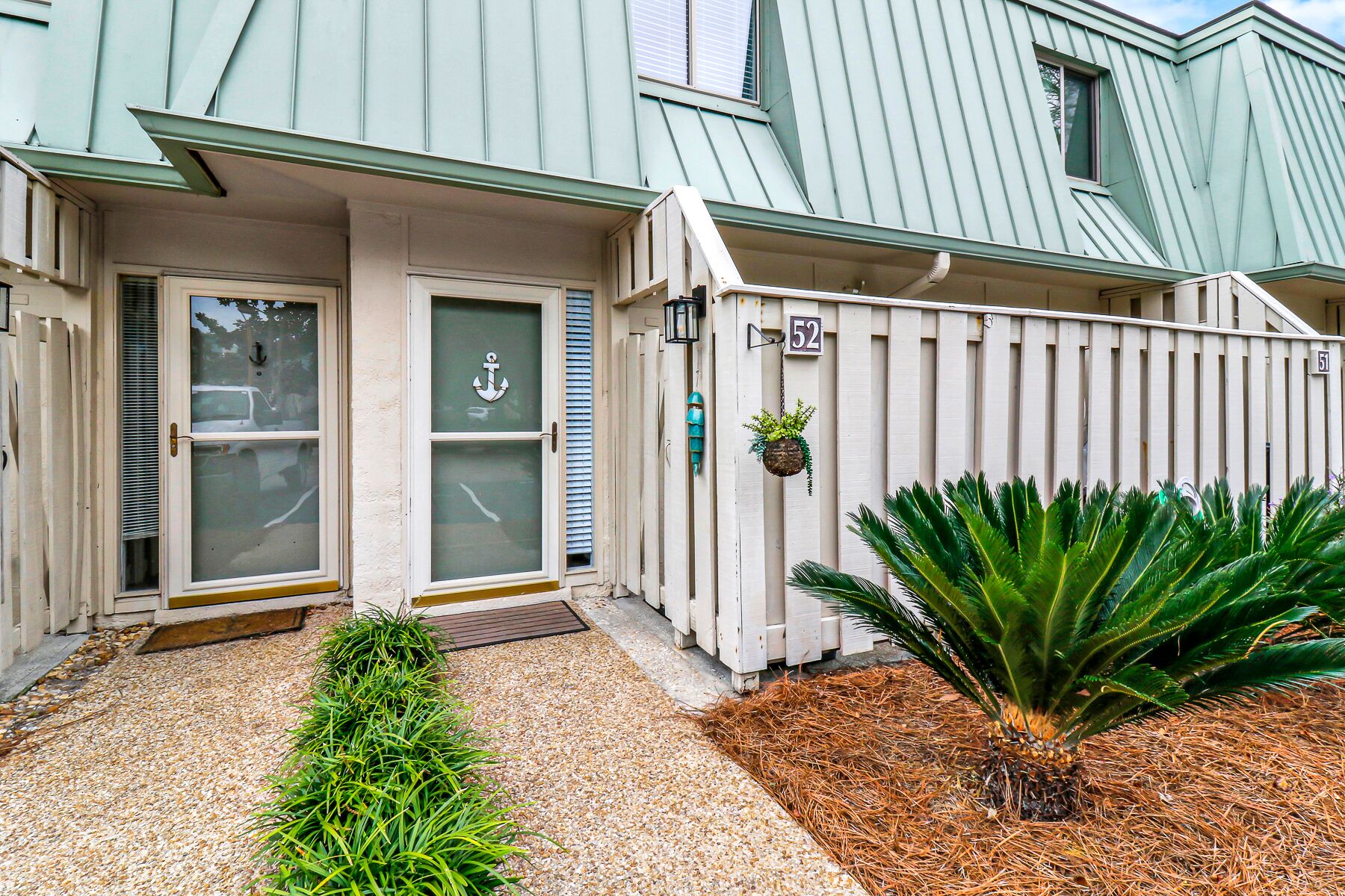 A house with a white picket fence, a small garden with a palm tree, and a door with an anchor symbol.