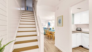 A staircase leading to a dining area with wooden flooring, white walls, and a kitchen with white cabinets. - Pet Friendly Beachside Villa - Across the Street from the Beach! (Hilton Head Island)
