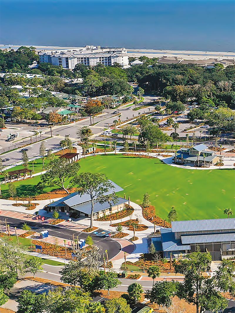 A resort with a large green lawn, a parking area, and a view of the ocean.
