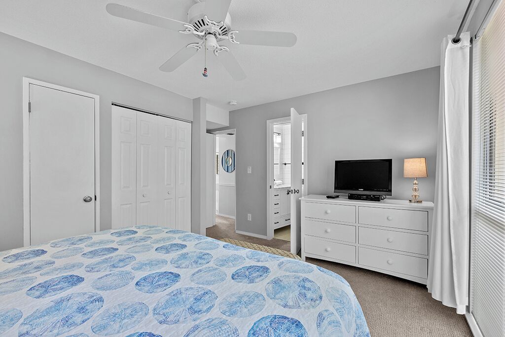 A bedroom with a bed, a ceiling fan, a TV, and a dresser.