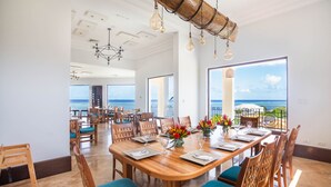 A spacious dining area with a large wooden table, chairs, and a view of the ocean. - Pristine Bay Villa 1304 with large pool - 3 bedroom 3 Condo by RedAwning (Roatan)