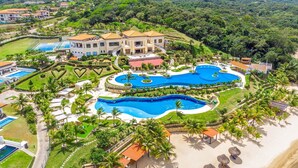 A resort with multiple swimming pools, palm trees, and a large building with a red roof. - Pristine Bay Villa 1304 with large pool - 3 bedroom 3 Condo by RedAwning (Roatan)