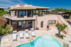 Una casa moderna de dos pisos con piscina, mobiliario exterior y un porche cubierto.