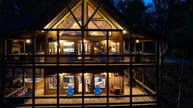 A two-story log cabin with a large central deck, multiple windows, and a hot tub on the ground floor. - Luxury Mountain Cabin for Families & Groups | 4 King Bedrooms + Hot Tub (Epworth)