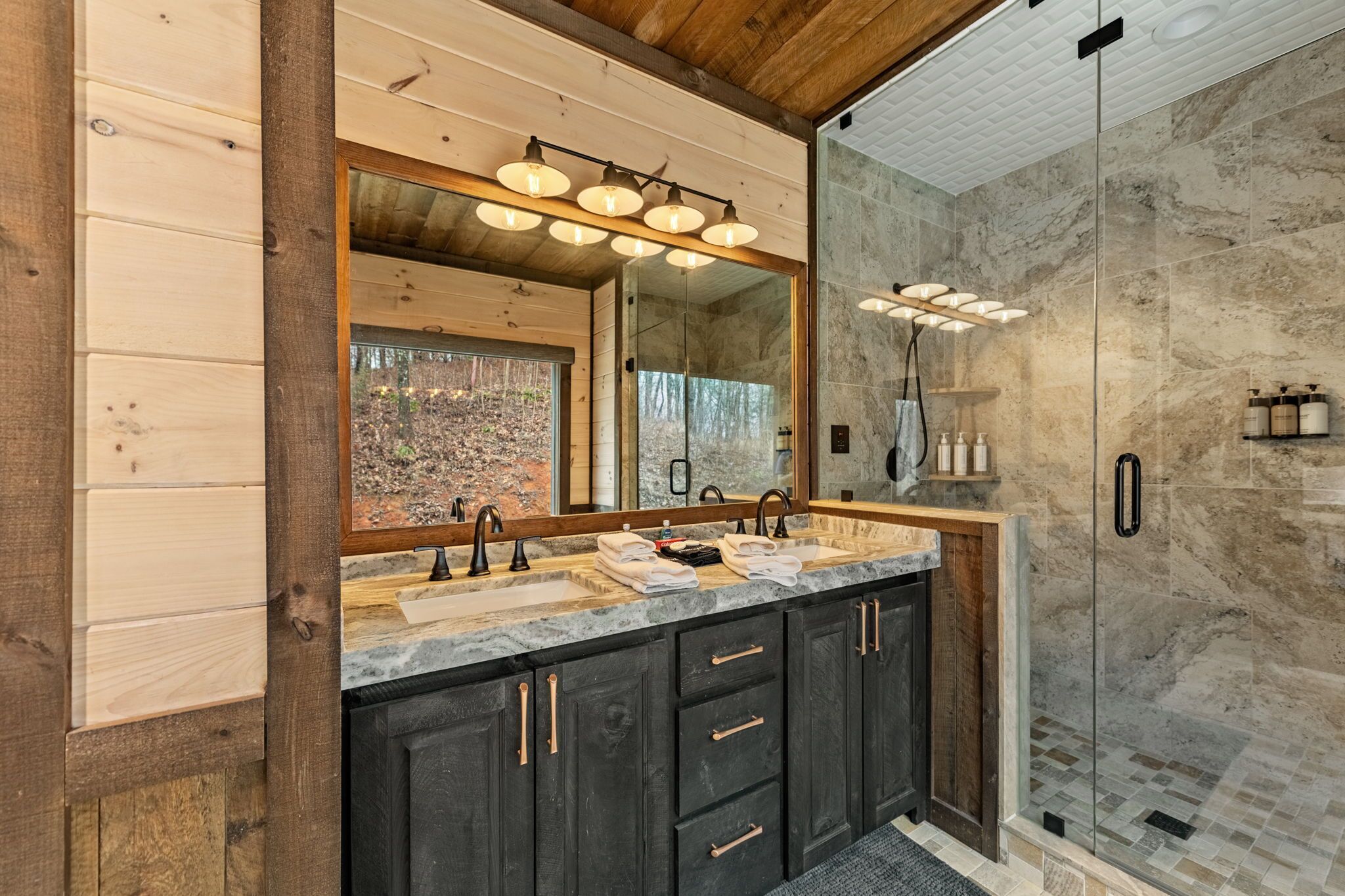 Un bagno moderno con arredamento in legno, un grande specchio, due lavabi e cabina doccia in vetro.