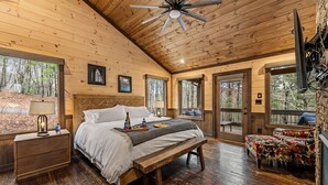 A wooden cabin bedroom with a bed, bedside table, lamp, and a bench. - Luxury Mountain Cabin for Families & Groups | 4 King Bedrooms + Hot Tub (Epworth)