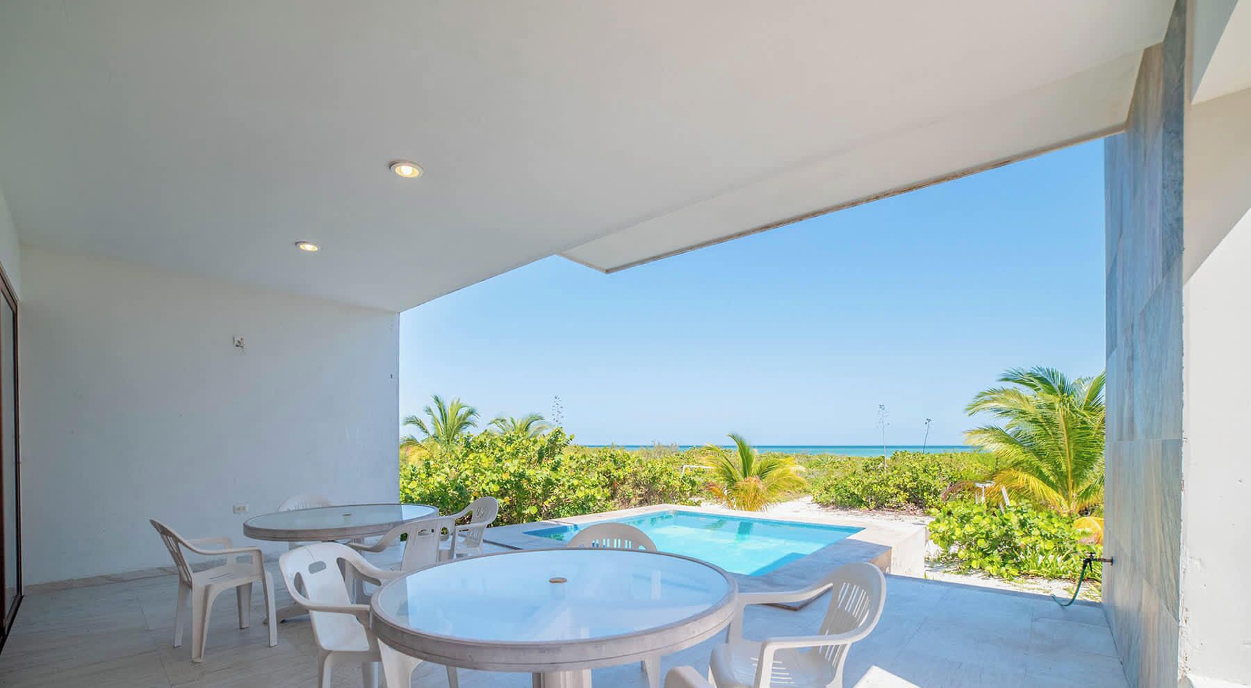 A modern outdoor area with a pool, white plastic chairs, and a view of the ocean.