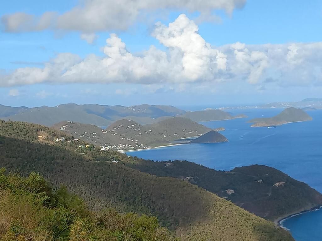 A coastal landscape with hills, a beach, and a clear sky.