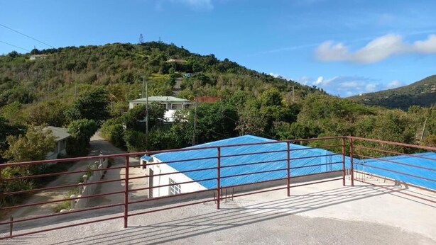 Un entorno rural con un edificio de techo azul, una valla de metal rojo y un paisaje montañoso al fondo.