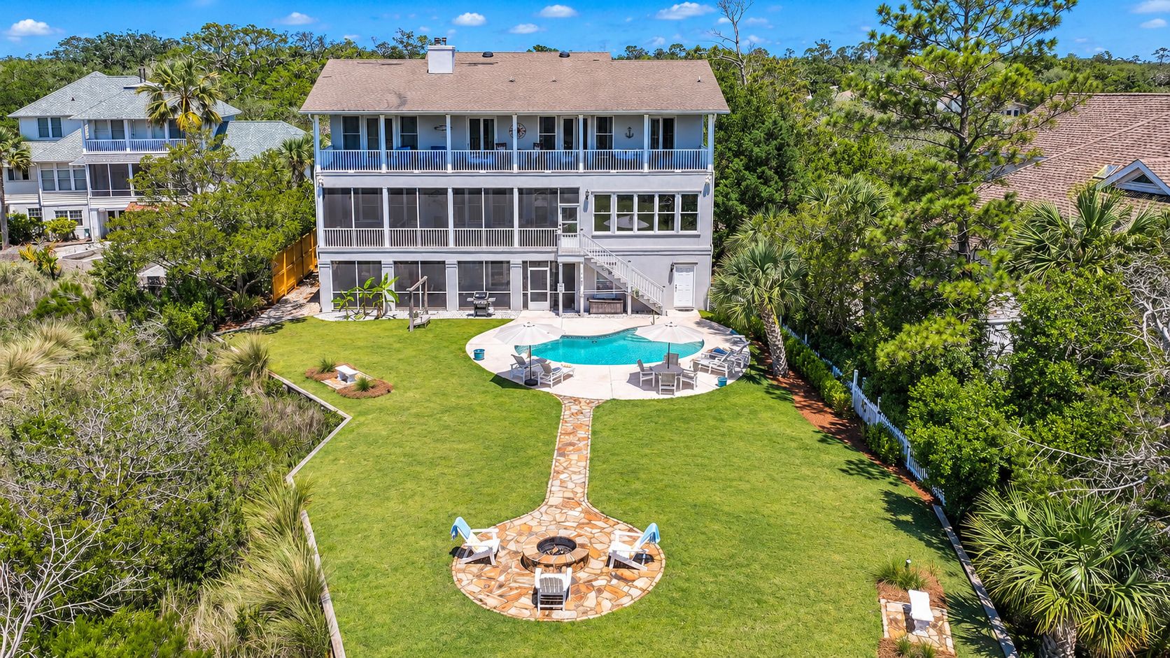 A two-story house with a swimming pool, a patio with outdoor furniture, and a well-maintained lawn.
