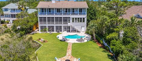 A two-story house with a swimming pool, a patio with outdoor furniture, and a well-maintained lawn.