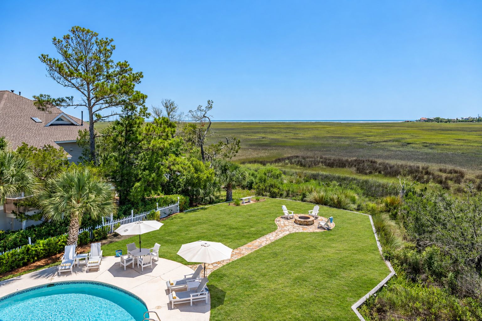 Ein Garten mit Swimmingpool, Liegestühlen, einer Feuerstelle und Blick auf den Ozean.