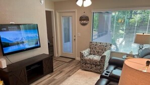 A living room with a flat-screen TV, a patterned armchair, a leather sofa, and a lamp.