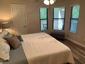 Un dormitorio con cama, mesita de noche, lámpara y ventana con persianas.