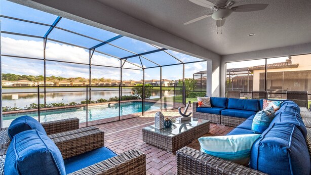 A covered outdoor area with a pool, wicker furniture, and a view of a lake. - Last Minute Disney! Private Pool, Hot Tub, Game Room & Themed Bedrooms. Book Now! #56669 (Orlando)