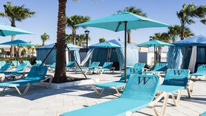 A poolside area with blue lounge chairs and umbrellas, palm trees, and a tiled floor. - Last Minute Disney! Private Pool, Hot Tub, Game Room & Themed Bedrooms. Book Now! #56669 (Orlando)
