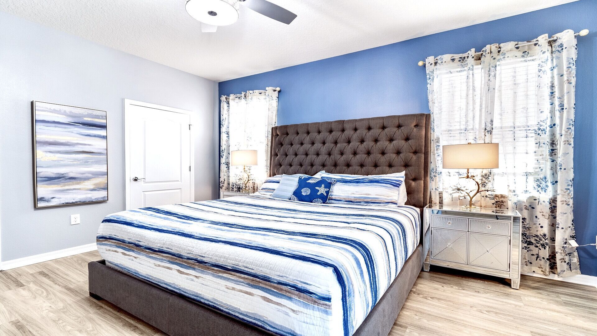 A bedroom with a large bed, a nightstand, a ceiling fan, and a wall-mounted artwork.
