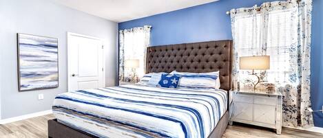 A bedroom with a large bed, a nightstand, a ceiling fan, and a wall-mounted artwork.
