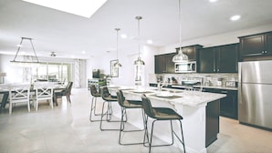 Une cuisine moderne dotée d’un îlot central, de meubles de couleur sombre, d’appareils électroménagers en acier inoxydable et de luminaires suspendus.