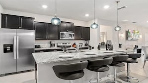 Cocina moderna con armarios oscuros, electrodomésticos de acero inoxidable, encimera de granito y taburetes de bar.