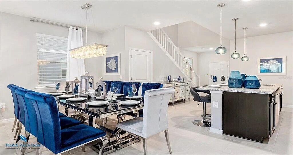 A modern dining area with a glass table, blue upholstered chairs, and a black island counter.