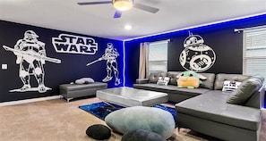 A Star Wars-themed room with a grey sofa, a gaming console, and Star Wars wall decals.