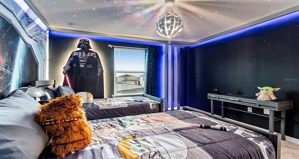A bedroom with a Star Wars theme, including a Darth Vader poster, a Star Wars character figure, and a galaxy-themed ceiling light.