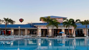 Ein Hotel mit Schwimmbad, Palmen und einem Heißluftballon am Himmel.