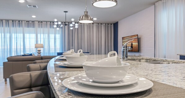 A modern kitchen with a marble countertop, a dining area with a sofa, and a large window with curtains.