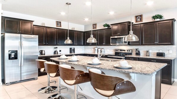 A modern kitchen with dark cabinets, stainless steel appliances, a granite countertop, and bar stools.
