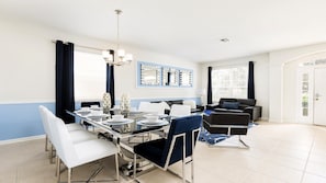 A modern dining area with a glass table, white chairs, and blue curtains. - Last Minute Disney! Private Pool, Hot Tub, Game Room & Themed Bedrooms. Book Now! #56625 (Orlando)